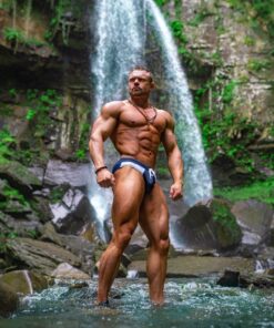 A bodybuilder stood by a waterfall wearing Nefertiti Swimwear trunks.